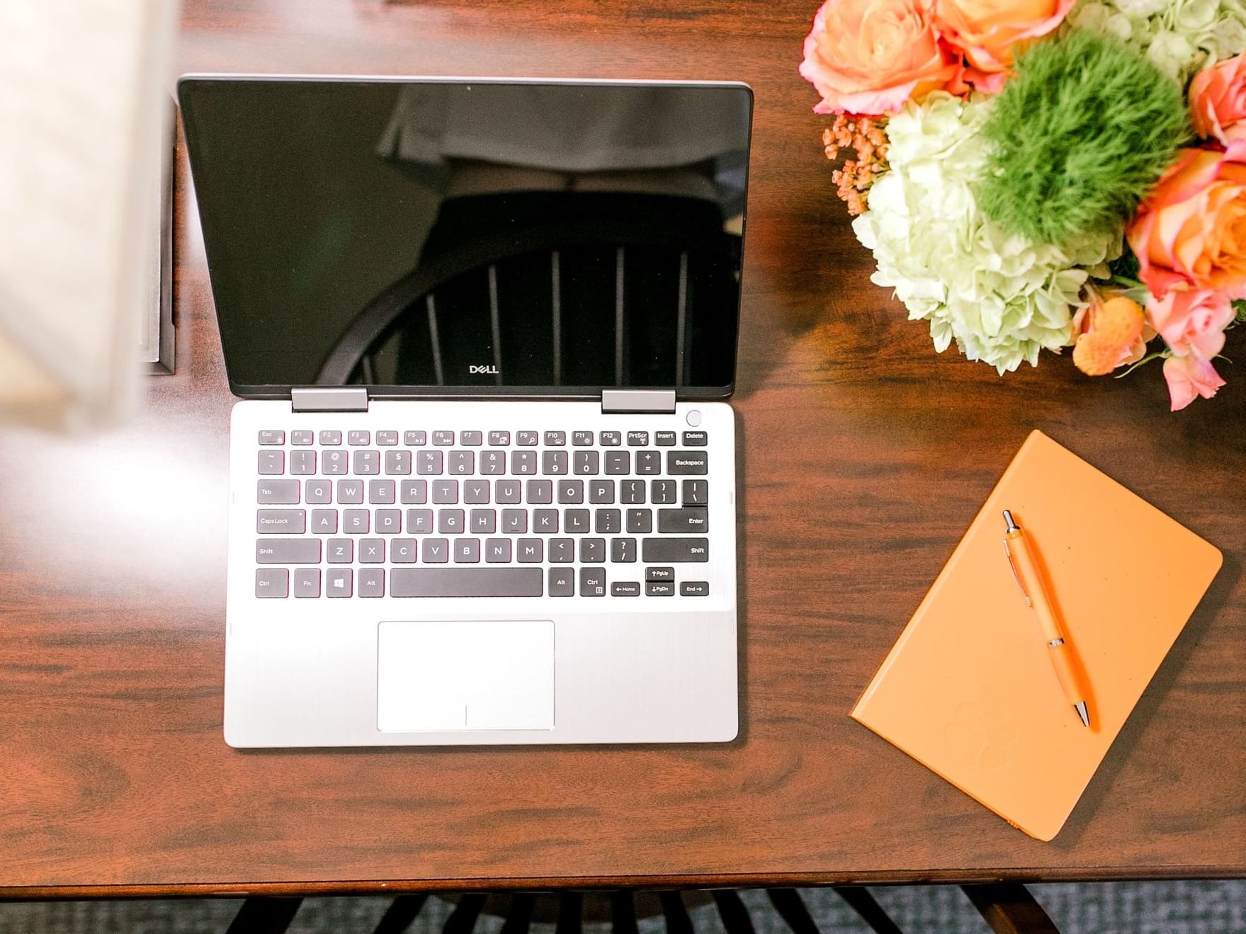 Laptop, notepad with pen, and flowers on tabletop