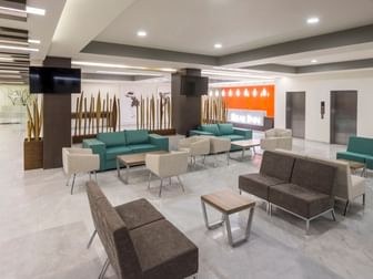 Spacious lobby with teal and brown seating, marble floors, and decorative wood pillars at Real Inn Celaya
