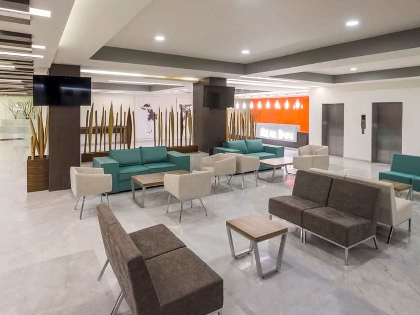 Spacious lobby with teal and brown seating, marble floors, and decorative wood pillars at Real Inn Celaya