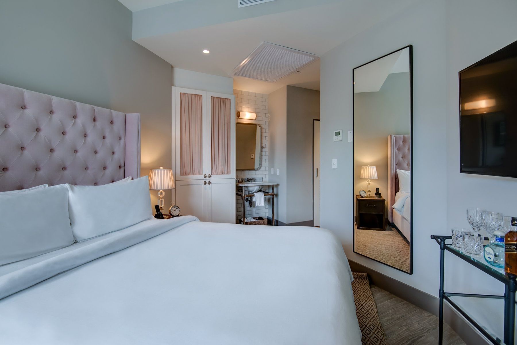 A wide-angle view of a hotel room with a king-sized bed, dresser, and flat-screen TV.
