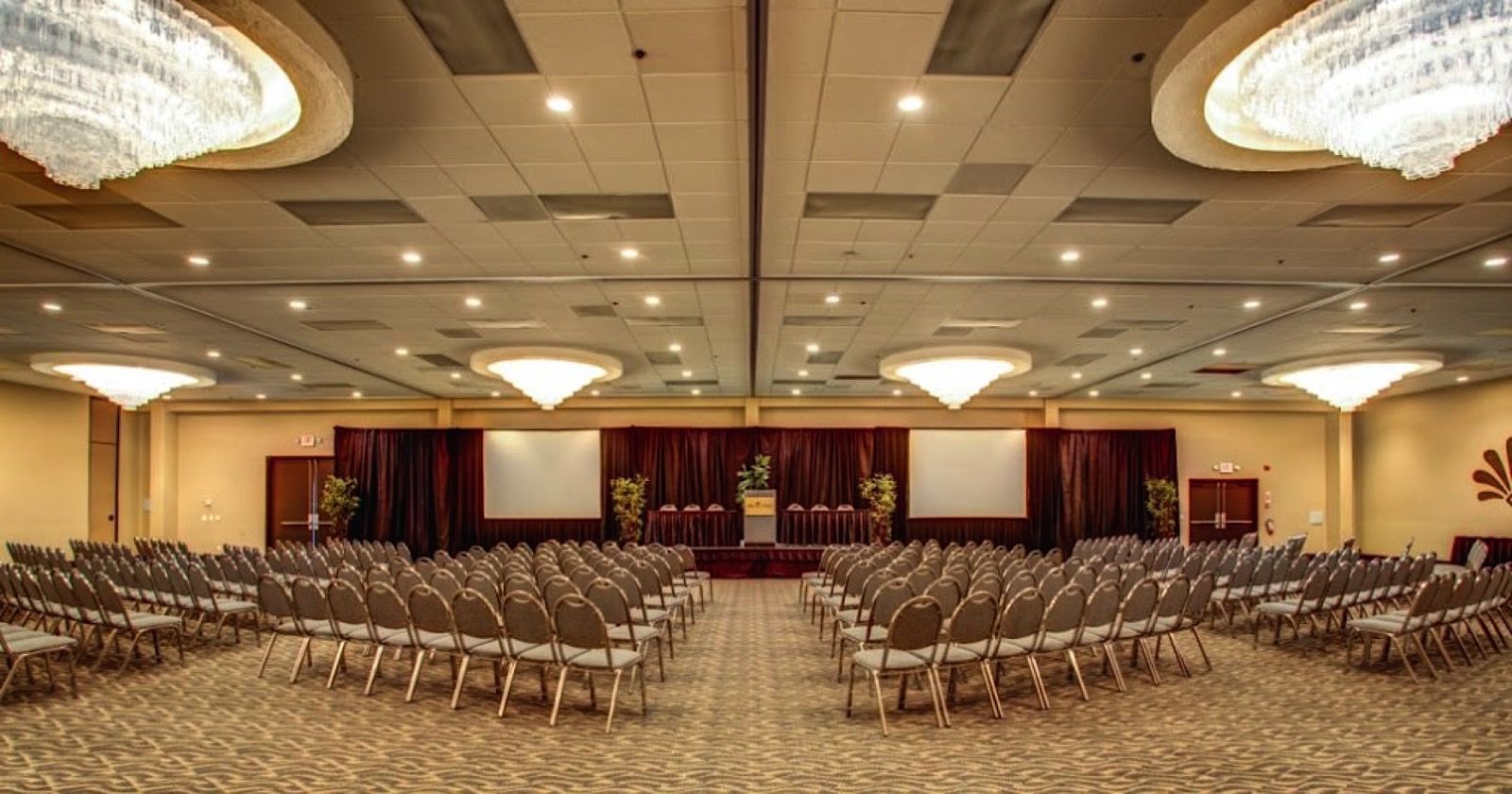 A large meeting room with rows of chairs facing a stage with curtains and boards.