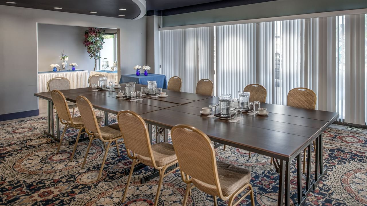 A conference room with a long table, chairs, floral centerpieces, and large windows with blinds.