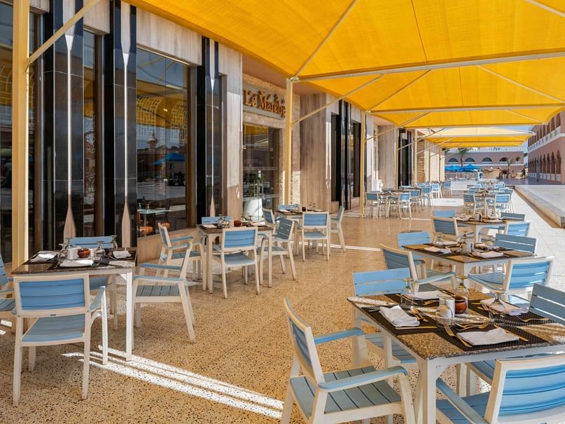 Outdoor dining area with blue chairs under yellow awnings at Le Marché in Red Sea Governorate.