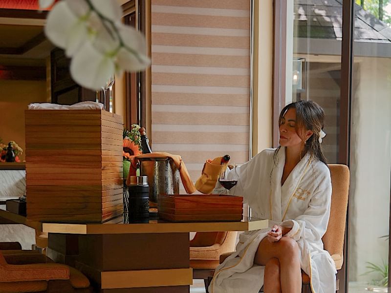 Woman in a bathrobe seated at a table with wine and canapes promoting festive season long stay