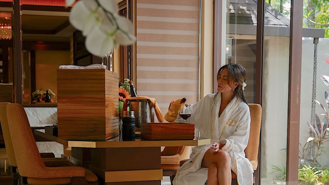 Woman in a bathrobe seated at a table with wine and canapes promoting festive season long stay