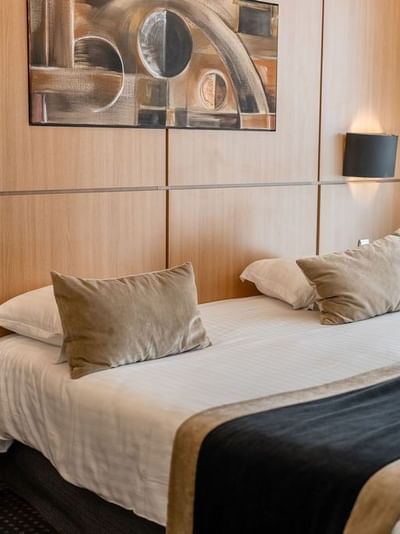 Chambre d'hôtel avec lit, deux oreillers, lampes murales, téléphone, peinture, et rideau.