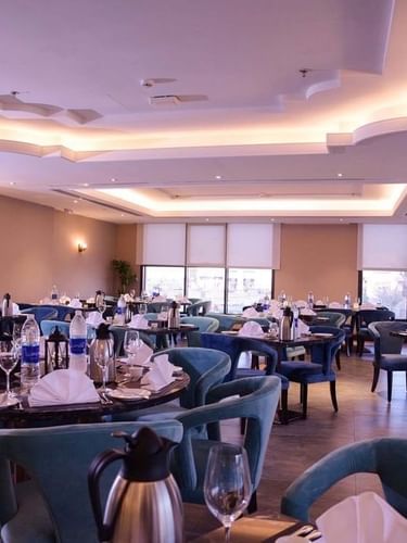 Al Multaqa Restaurant with blue velvet chairs by round tables under soft, warm lighting at Warwick Al Khobar