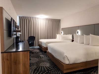 Two beds, desk with chair, and TV in a hotel room at Carriage House Hotel & Conference Centre