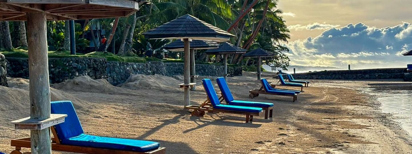 Sandy beach with lounge chairs under umbrellas at Warwick Fiji Resort and Spa in Korolevu