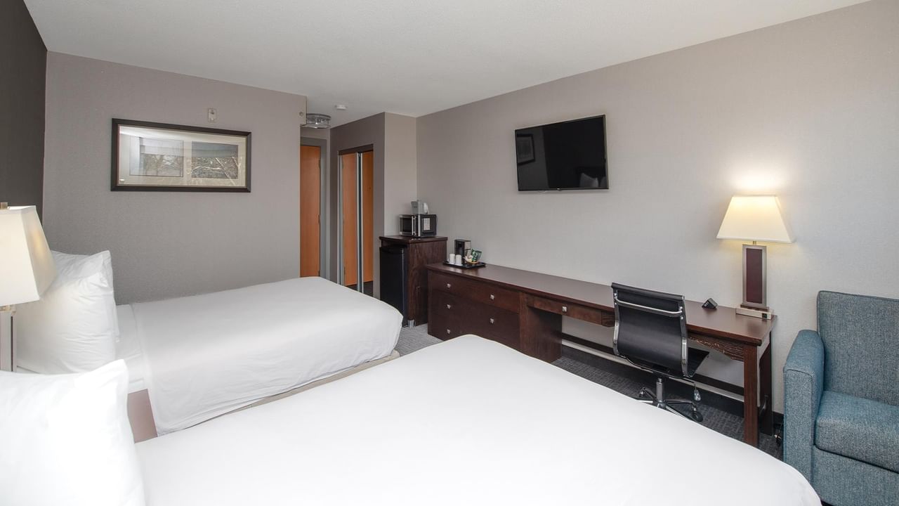 Two beds, desk, TV, and chair in a hotel room.