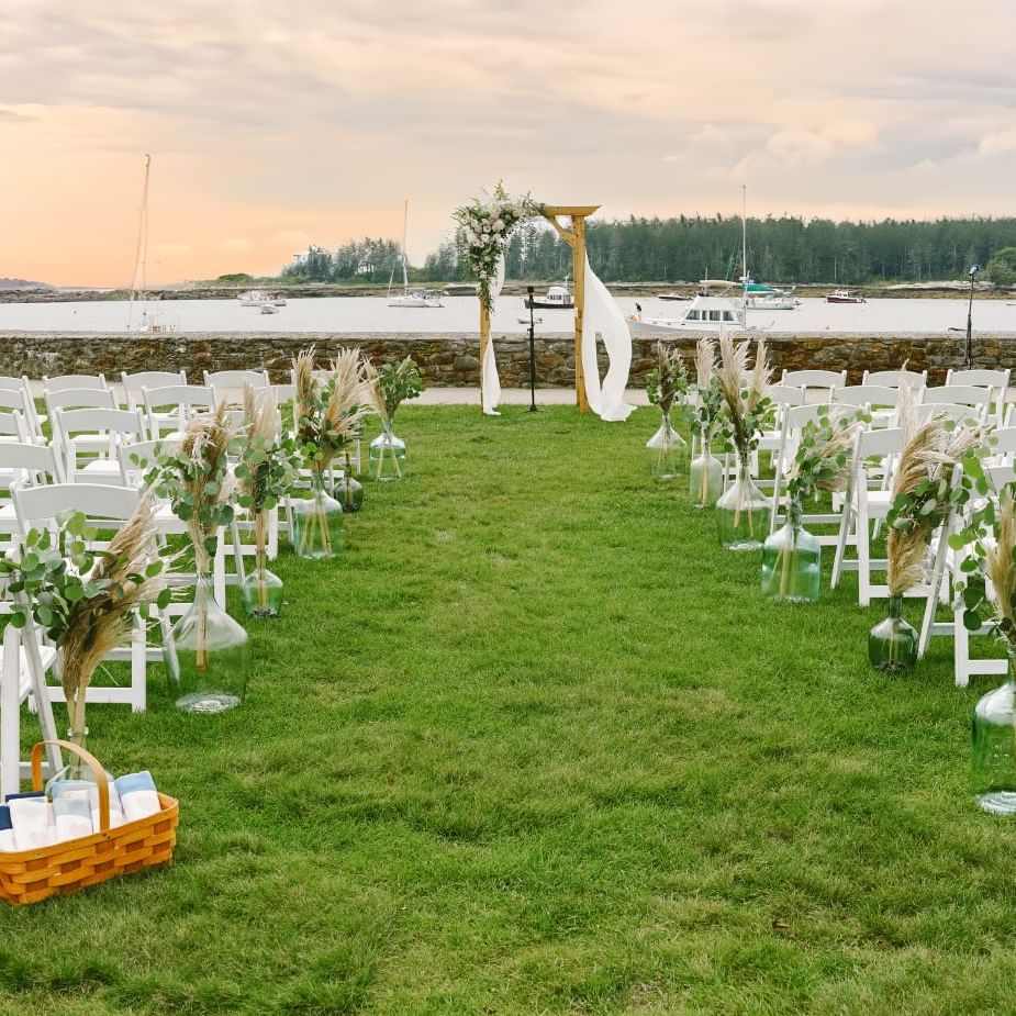 Outdoor wedding ceremony set up with white chairs facing a wooden arch at Ogunquit Collection