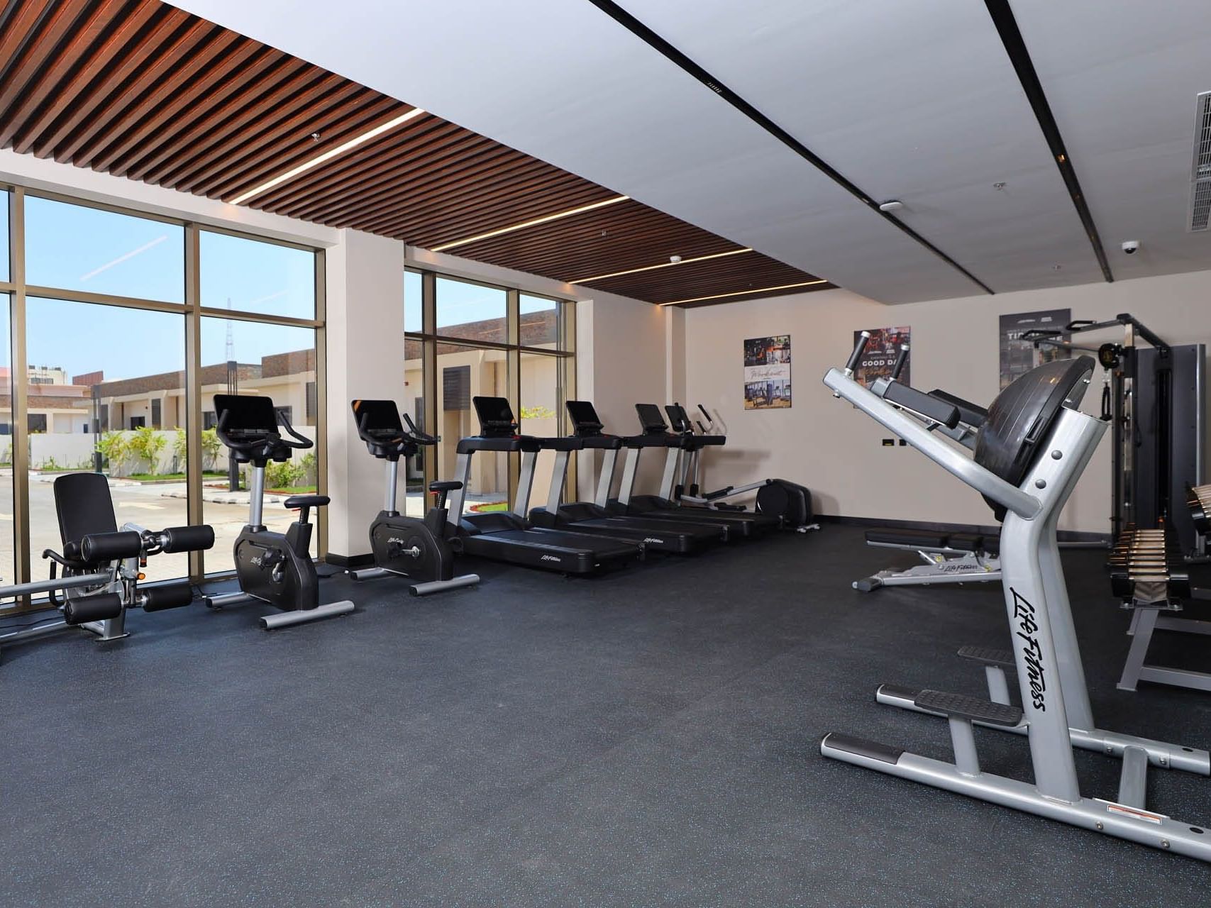 Modern gym with treadmills, stationary bikes, and weight machines in a well-lit room with large windows.