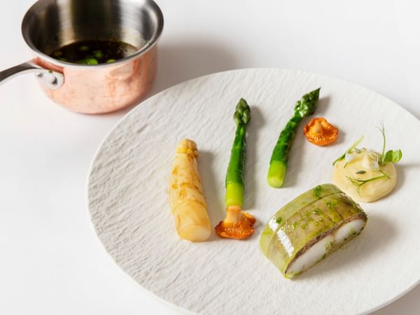 Plate with asparagus, mushrooms, and other garnishes next to a copper pot with sauce.