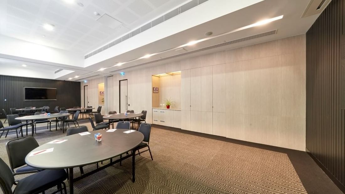 Round tables set up with chairs facing a large projection screen in The Think Tank at Ibis Adelaide
