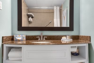 Bright bathroom at The Riverwalk Plaza Hotel with a granite countertop, towels, and a mirror reflecting the shower area