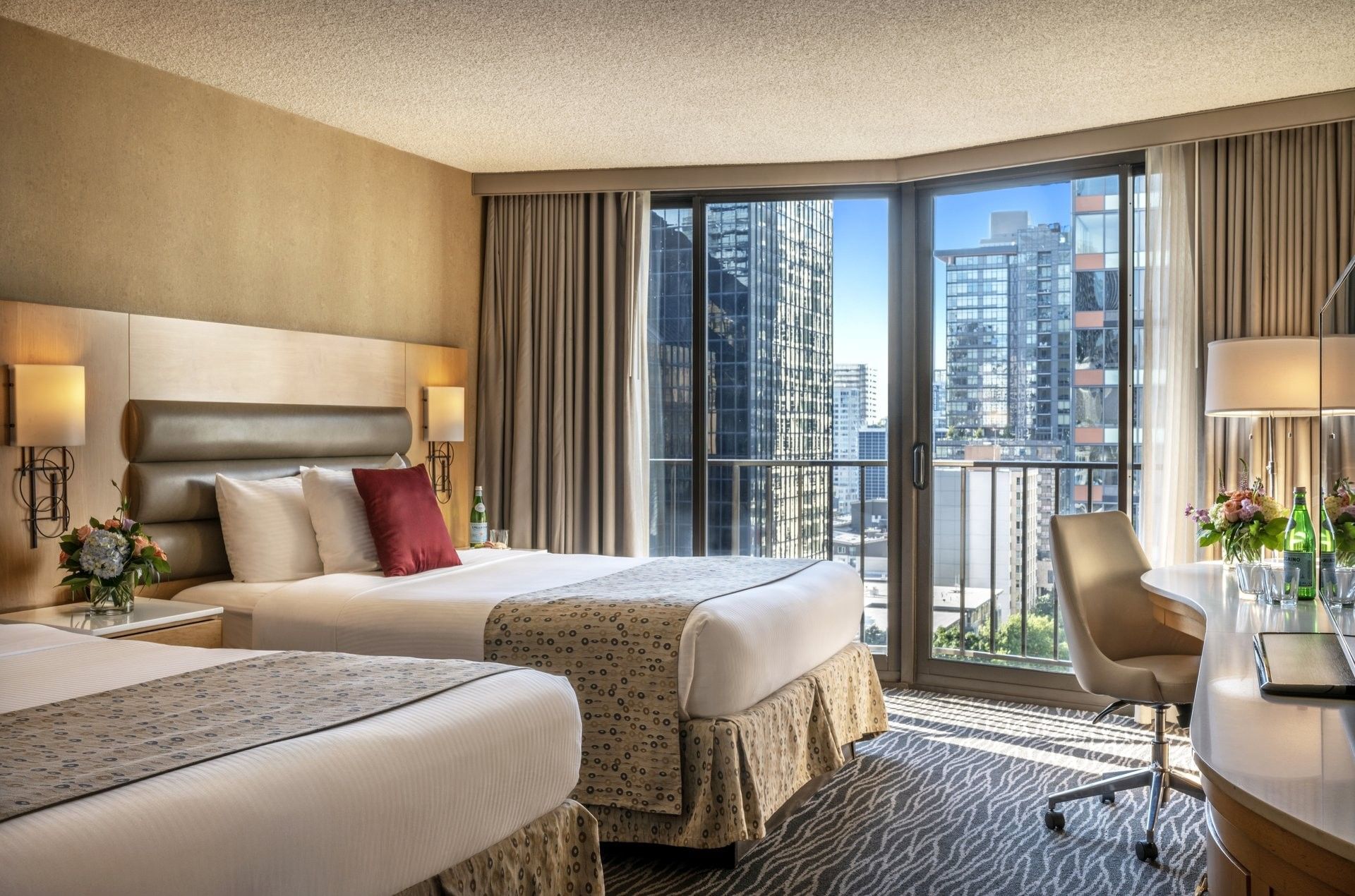 Two queen beds featuring red pillows by floor-to-ceiling windows under soft light in Executive Room at Warwick Seattle