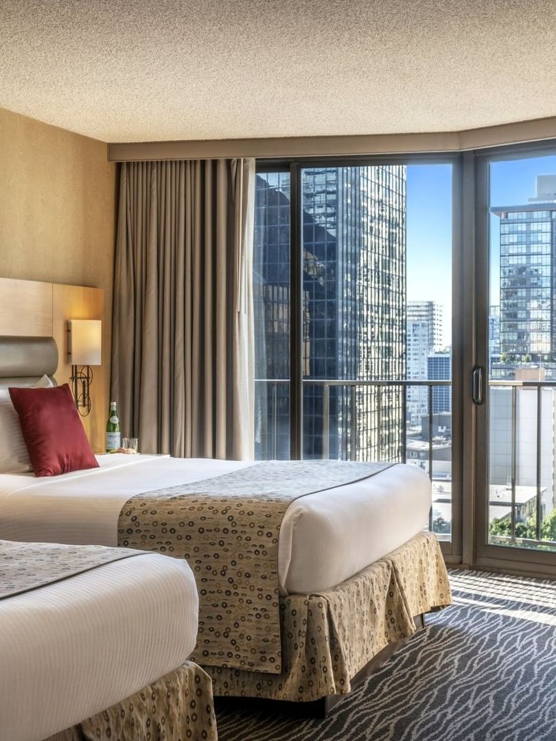 Two queen beds featuring red pillows by floor-to-ceiling windows under soft light in Executive Room at Warwick Seattle