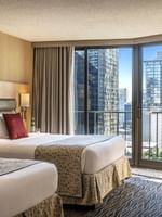 Two queen beds featuring red pillows by floor-to-ceiling windows under soft light in Executive Room at Warwick Seattle