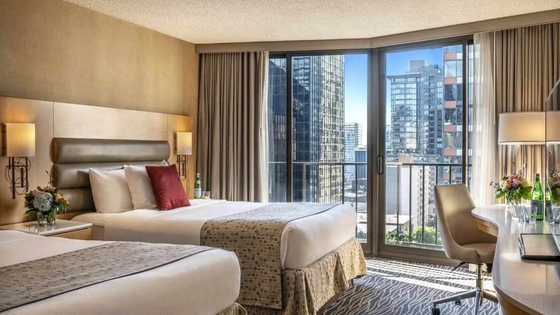 Two queen beds featuring red pillows by floor-to-ceiling windows under soft light in Executive Room at Warwick Seattle