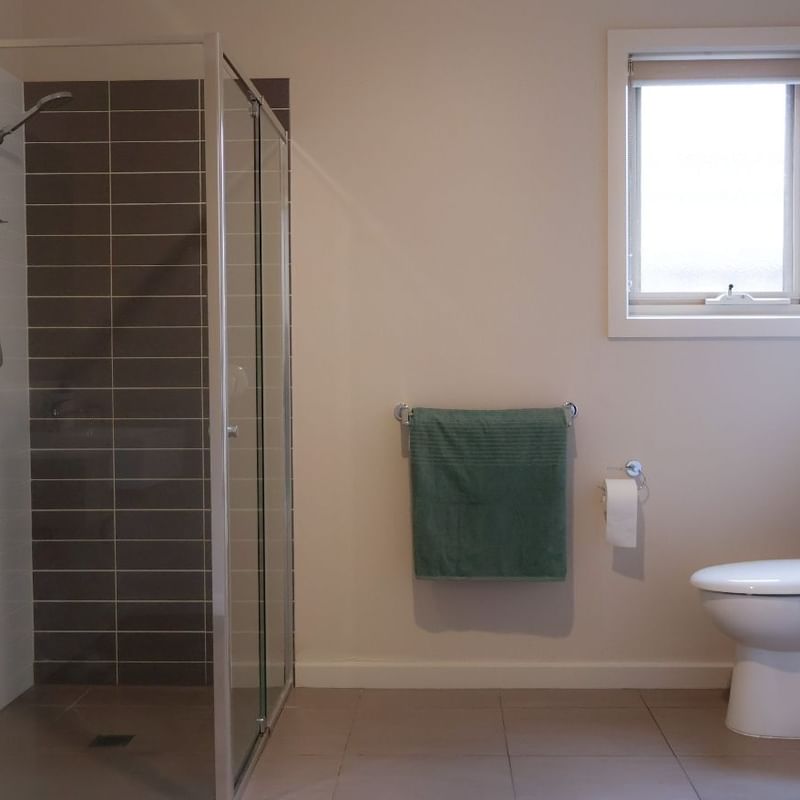 Green towels and white toilet next to glass shower in bathroom at La Trobe University Regional Housing – Melton.