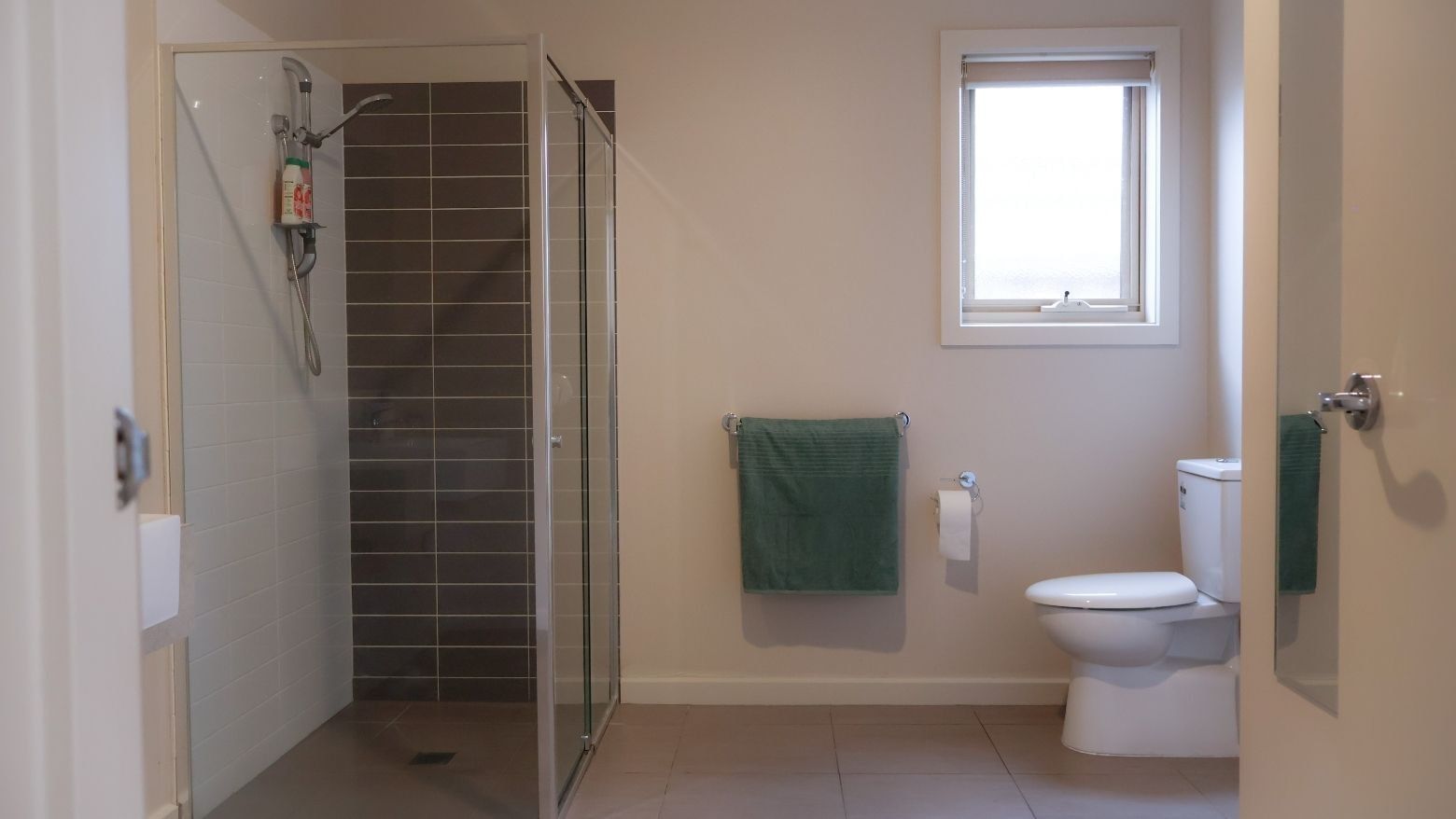 Green towels and white toilet next to glass shower in bathroom at La Trobe University Regional Housing – Melton.