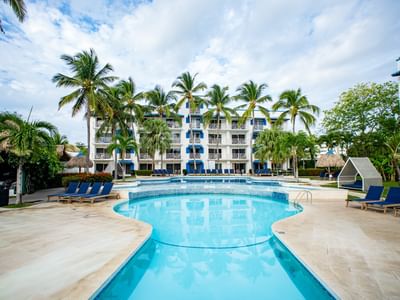 Multi-level pool with blue loungers surrounded by palm trees and white resort building at Playa Blanca Beach Resort