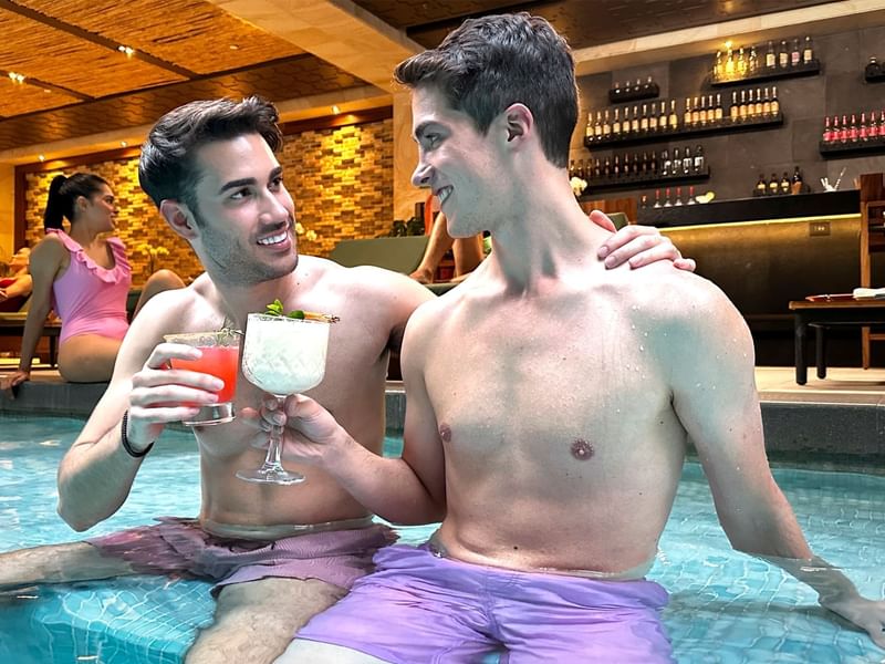 Two men relaxing in a pool with cocktails at Grand Fiesta Americana