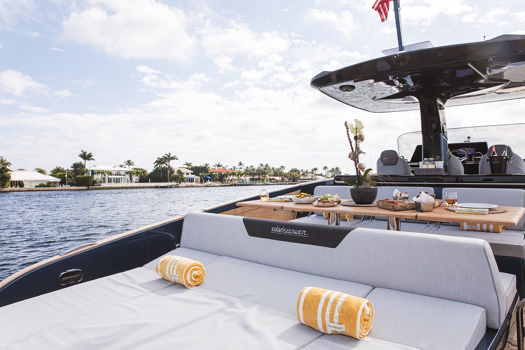 A yacht's deck with lounge seating, a table with food, and an American flag on the rear.