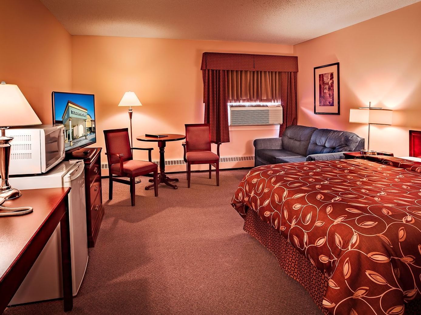 room with bed, sofa, accent chairs and table with television on dresser