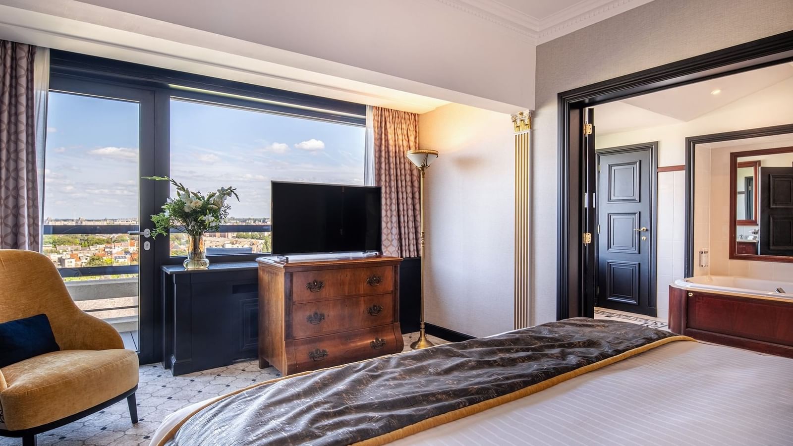 Elegant hotel suite with a city view and bed facing TV screen on wooden table at Hotel Barsey by Warwick