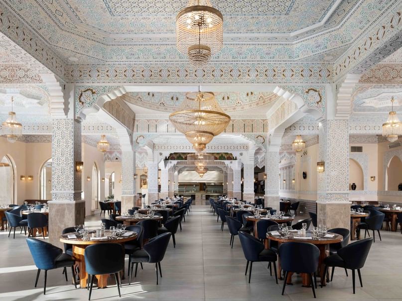 قاعة طعام أنيقة بطاولات وكراسي زرقاء وثريات معلقة من السقف المزخرف.