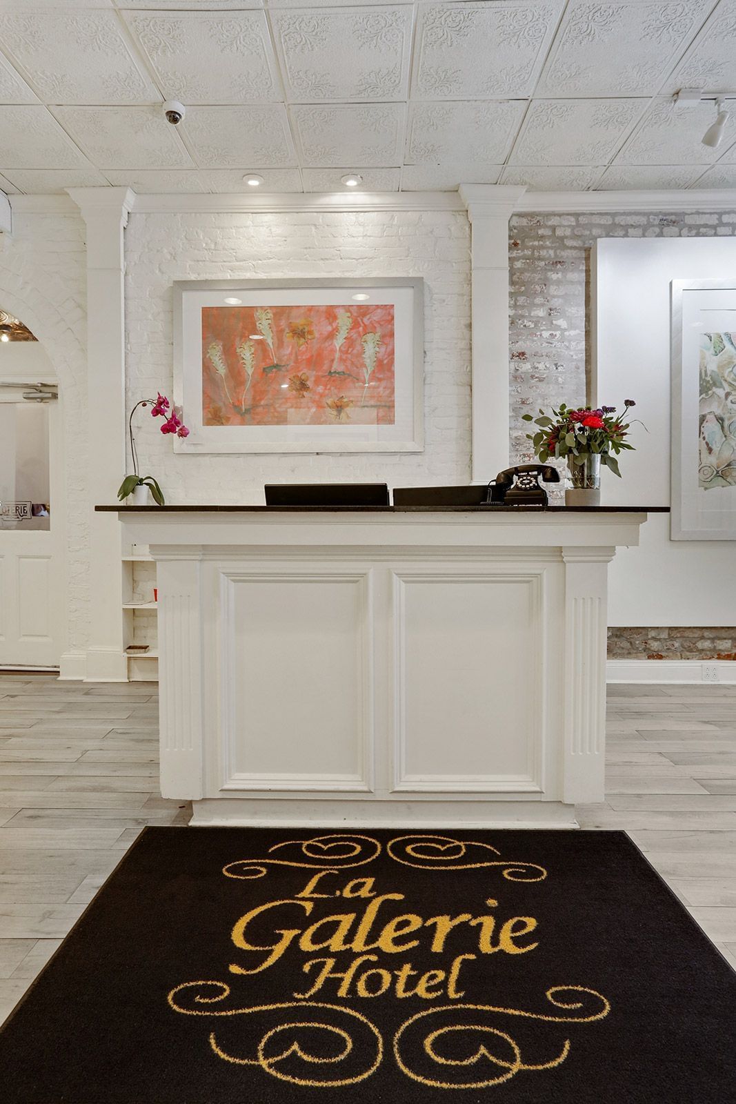 A hotel lobby with a white reception desk, artwork, flowers, and a rug.