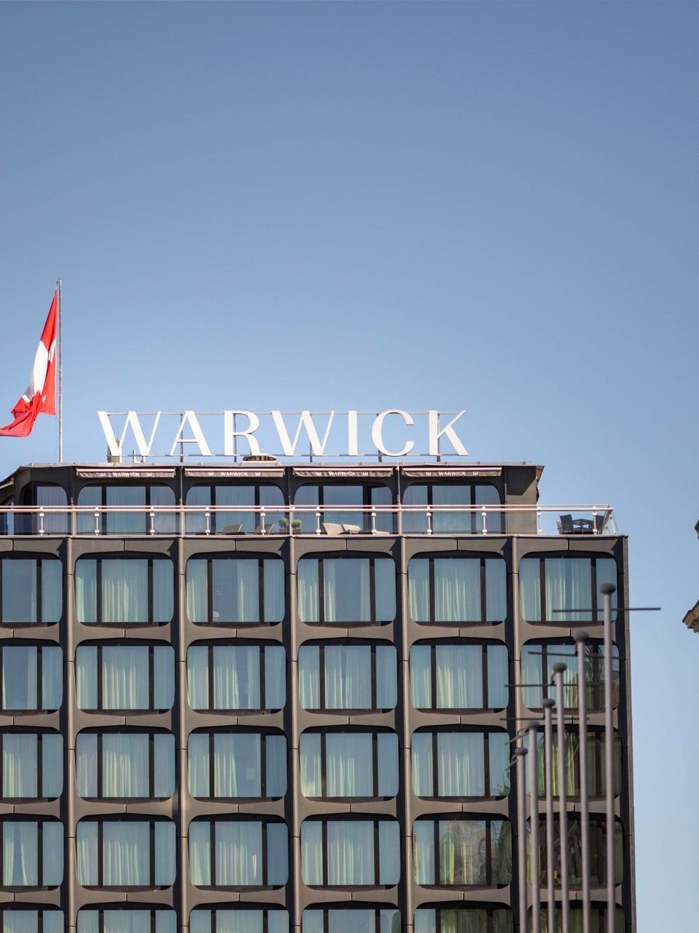 Exterior View of Warwick Geneva hotel with flag and rooftop signage under clear sky