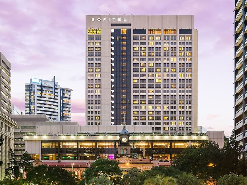 Sofitel Brisbane Central hotel facade at dusk with illuminated windows and a clock tower in the foreground