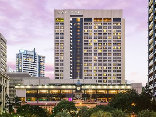 Sofitel Brisbane Central hotel facade at dusk with illuminated windows and a clock tower in the foreground