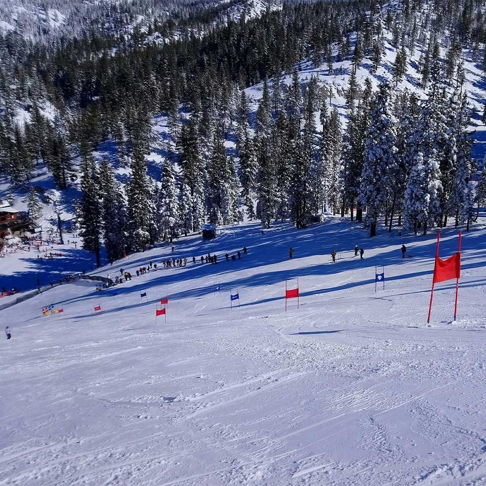 Snowy mountain slope with red flags and spectators for Lederhosen & Dirndl Parallel Giant Slalom.