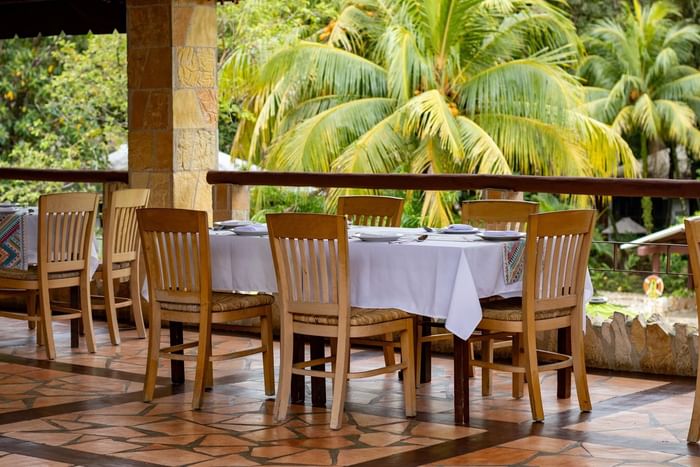 Restaurant tables with white linens and wooden chairs on a stone terrace at the Hotel Chan-kah Resort Village