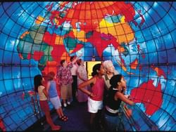 People of different ages stand inside a dome-shaped display with a colorful world map, examining it closely.