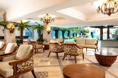 Elegant hotel lobby with patterned armchairs, stone columns, chandeliers, and pool view at Playa Los Arcos Puerto Vallarta
