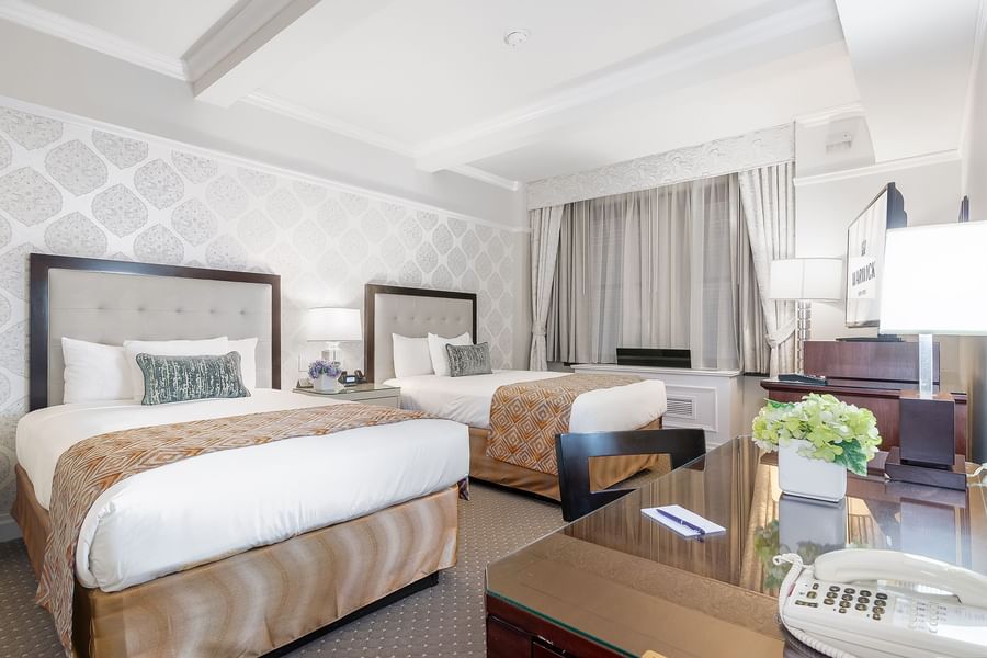 Twin beds with orange patterned runners facing TV with work desk area in Premier City View 2 Double beds at Warwick New York