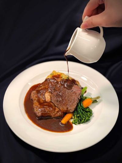 Close-up of gravy being poured over beef steak at York Hotel Singapore