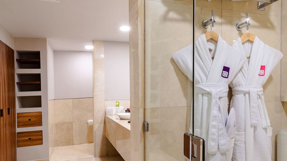 Pair of white bathrobes hanging on a marble wall in a King Master Suite bathroom at Camino Real Aeropuerto Mexico
