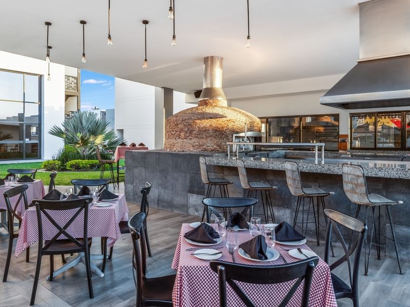 Solea Pizzería patio dining area with red checkered tablecloths and a large stone pizza oven backdrop at Sunvivia Mazatlán