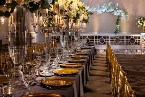 Elegant ballroom event setup with long tables, golden plates, candelabras, and floral decor at Warwick Hotels and Resorts