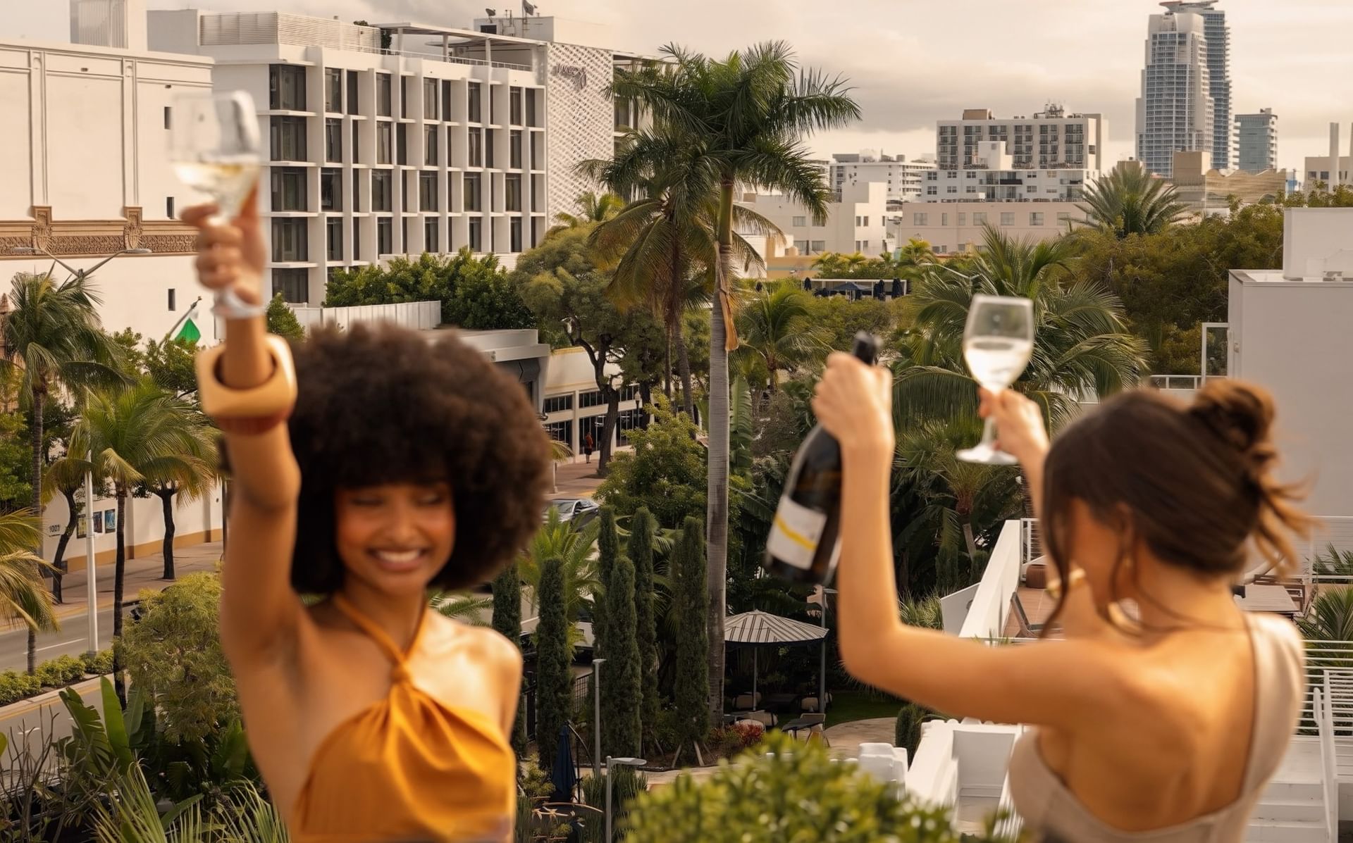 Two women toast with wine and champagne on a rooftop terrace and South Beach buildings at Kenmore Village Hotel, South Beach