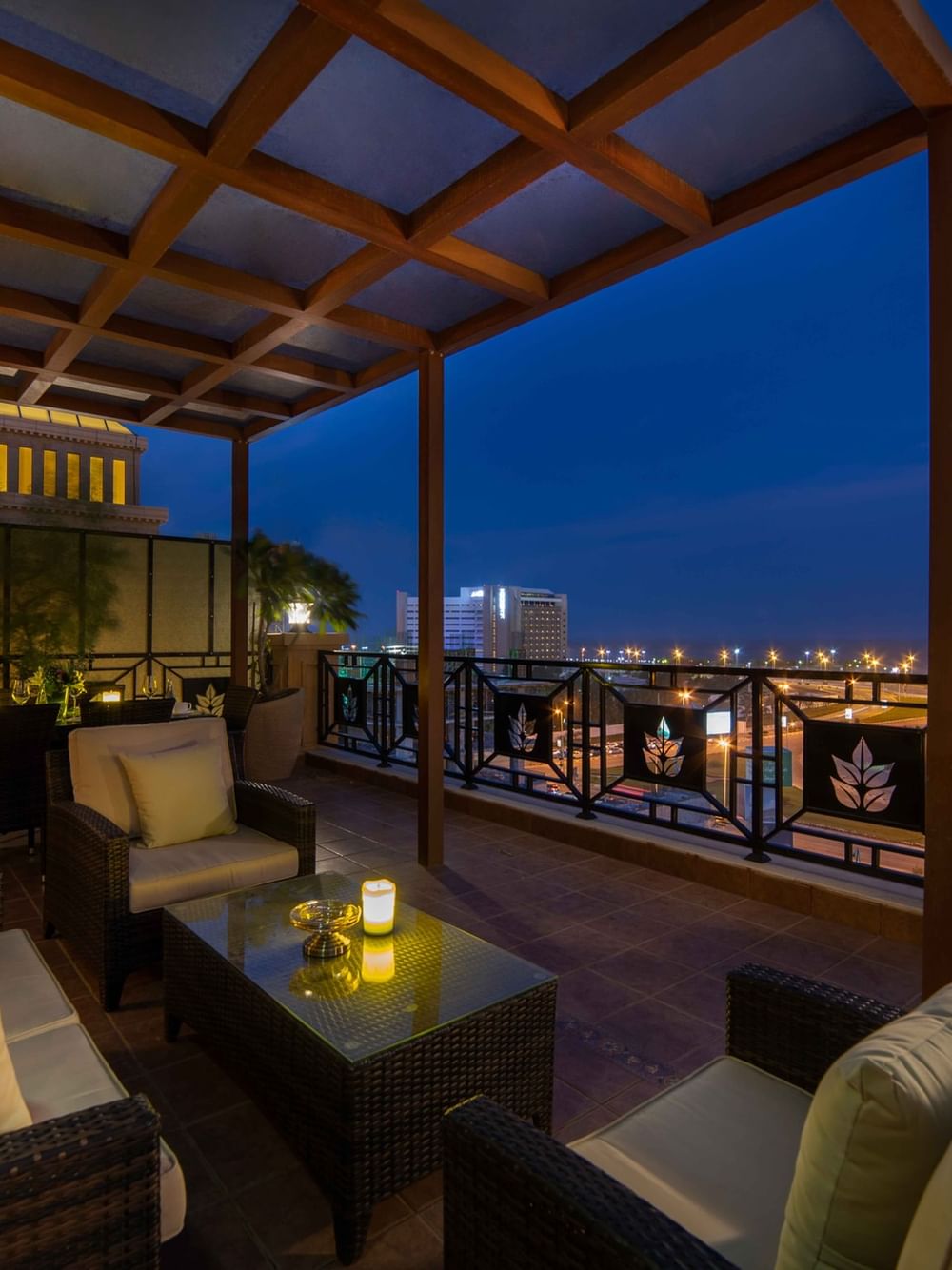 Wicker sofas by a glass coffee table under a glowing wooden canopy in Penthouse Villa at Warwick Al Khobar