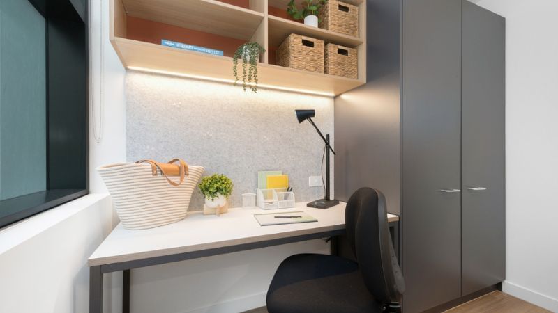 A neat study area with a desk, chair, large cabinet, and open shelving above.
