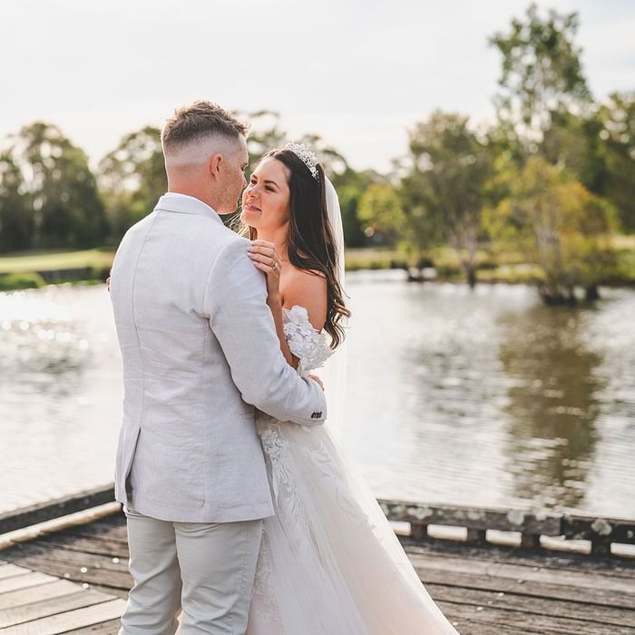 Wedding couple embracing on a jetty overlooking a tranquil lake near Mercure Kooindah Waters
