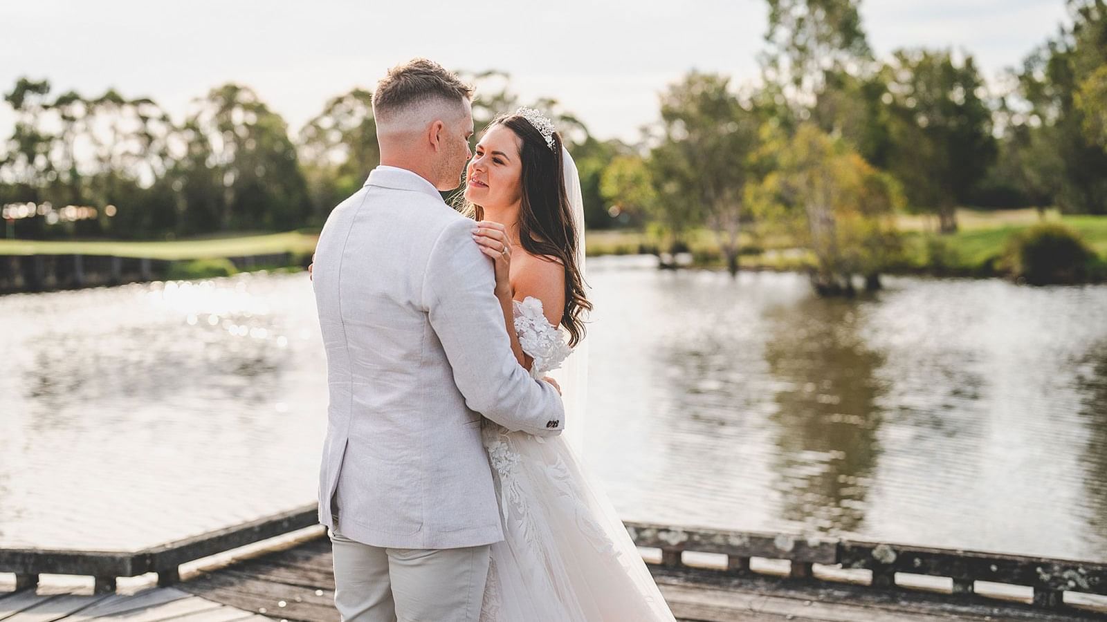 Wedding couple embracing on a jetty overlooking a tranquil lake near Mercure Kooindah Waters
