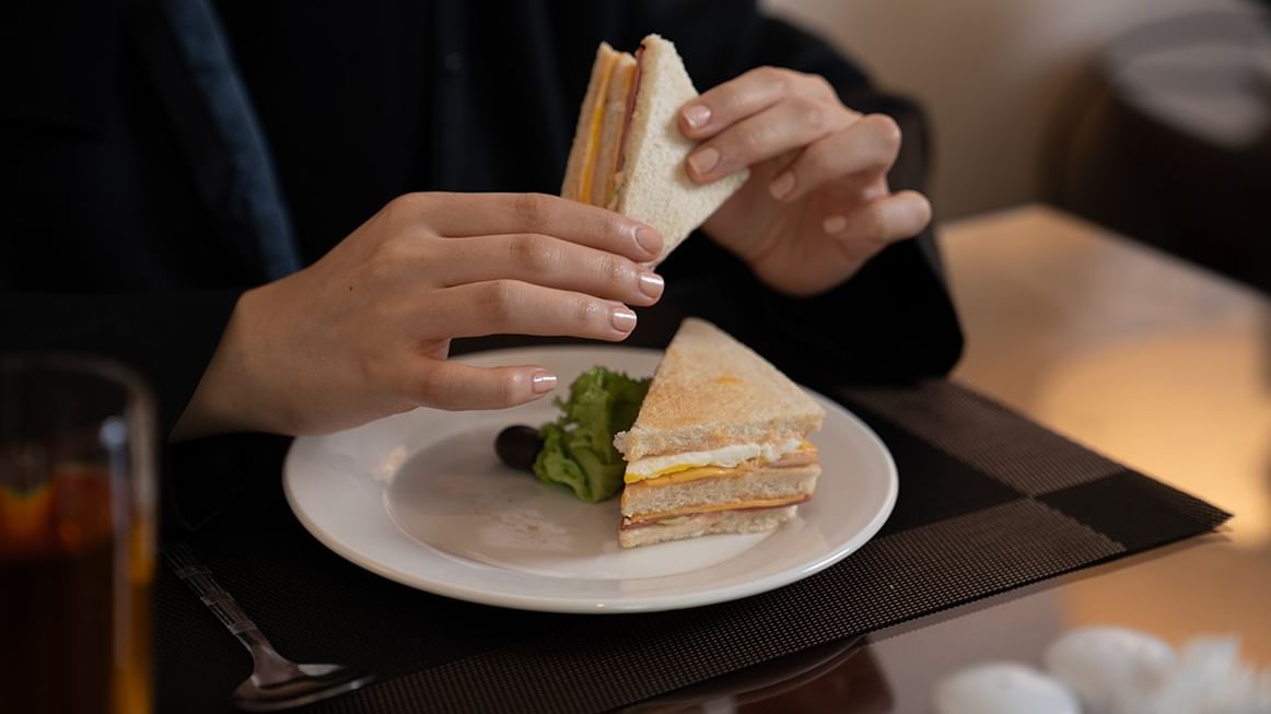 Woman dining with a sandwich and salad at Saja by Warwick Makkah.